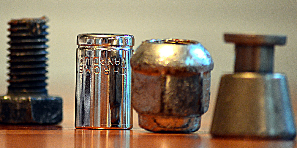 Four metail objects in a row; a bolt screw. bit socket, wheel nut, and an unidentified small object shaped like a bell.